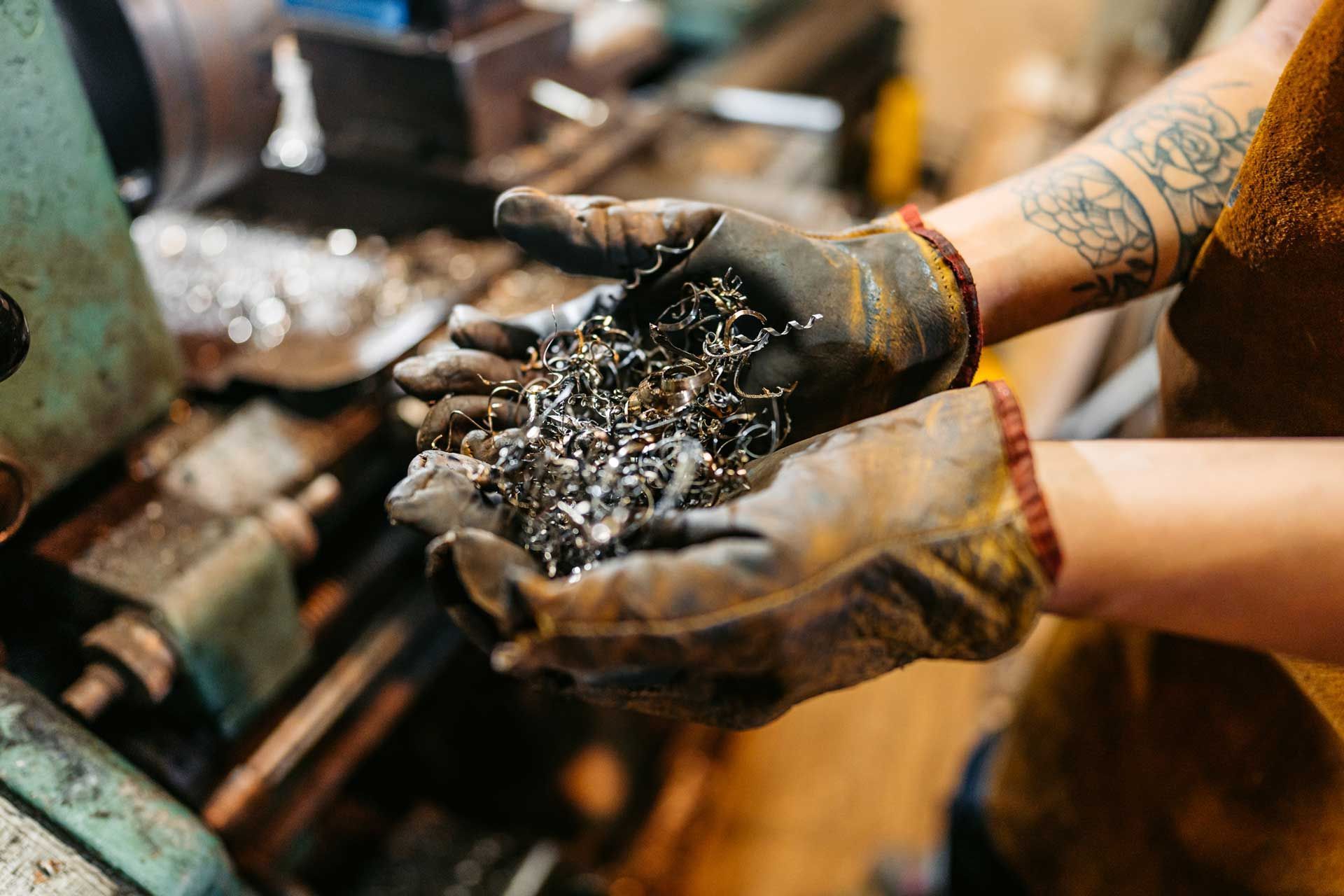 Gloved hands holding metal shavings in a workshop with machinery in the background