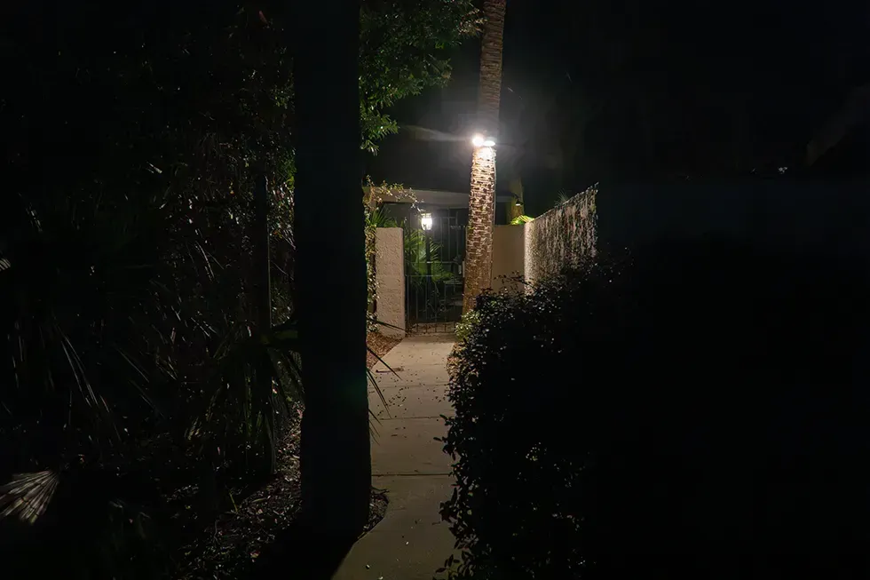 Dimly lit garden path leading to a brightly lit doorway at night