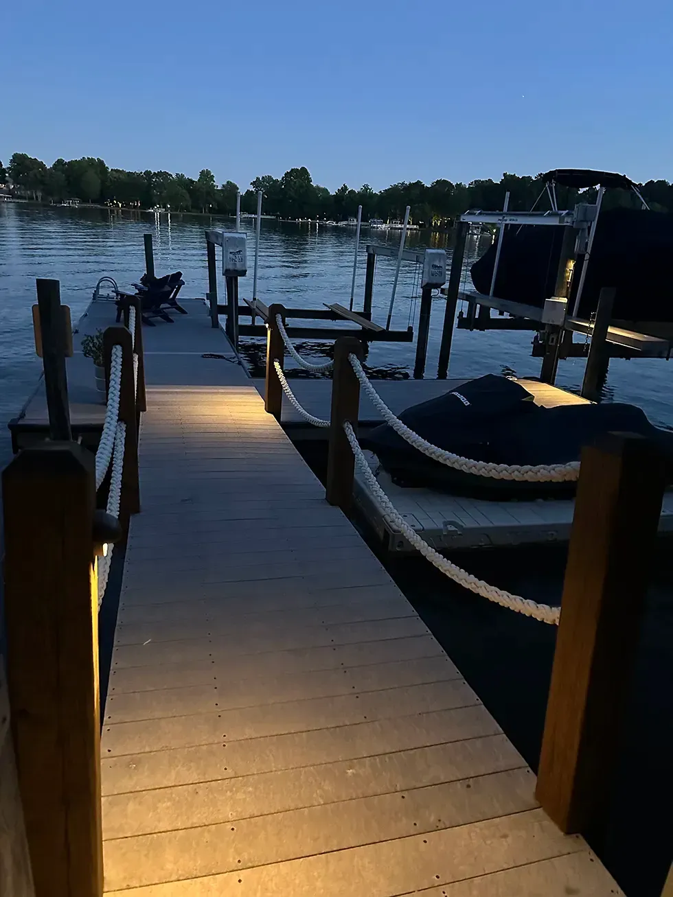 Wooden dock at dusk with boats moored on calm water, lit by warm dock lights