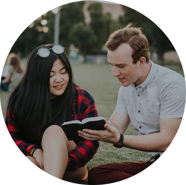 Two people sitting outdoors reading a book together