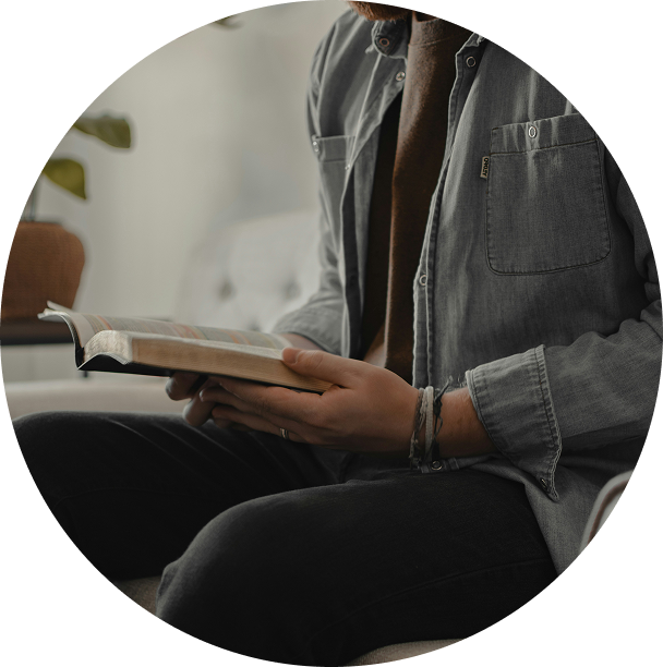 Person reading a book while seated indoors in a gray shirt and black pants