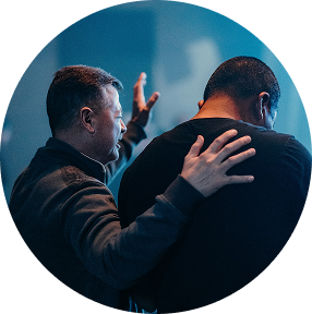 Two people in a blue-lit setting, one hand on the other's back in a supportive gesture.