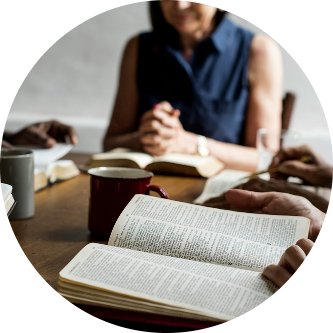 People studying together around an open book at a table, with mugs and notebooks.