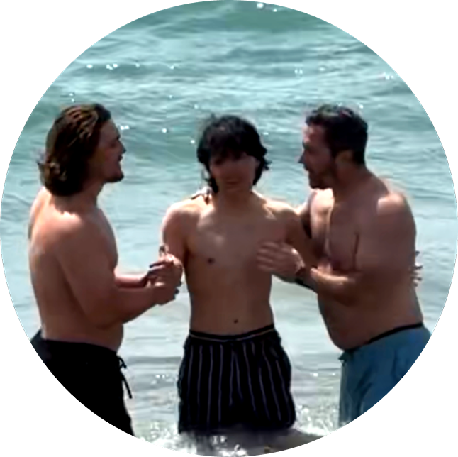 Three people standing in ocean surf, talking together at the beach.