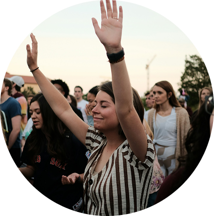 People with raised hands at an outdoor gathering at sunset