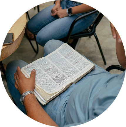 Person in a blue shirt reading an open book while seated indoors with others nearby