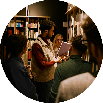 Small group reading together in a cozy library, one person holding a tablet and speaking.