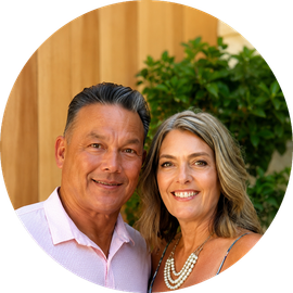 Smiling couple posing outdoors in front of a wooden wall and green foliage