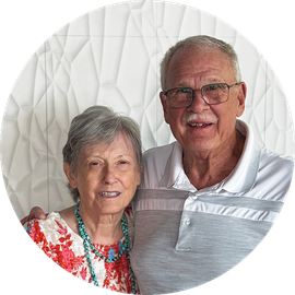 Smiling older couple posing closely together against a white textured wall.