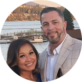 Smiling couple posing outdoors by a lake with mountains in the background at sunset