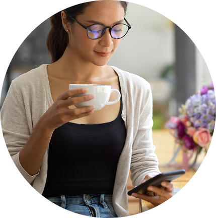 Woman in glasses holding a cup and checking her phone in a bright indoor setting