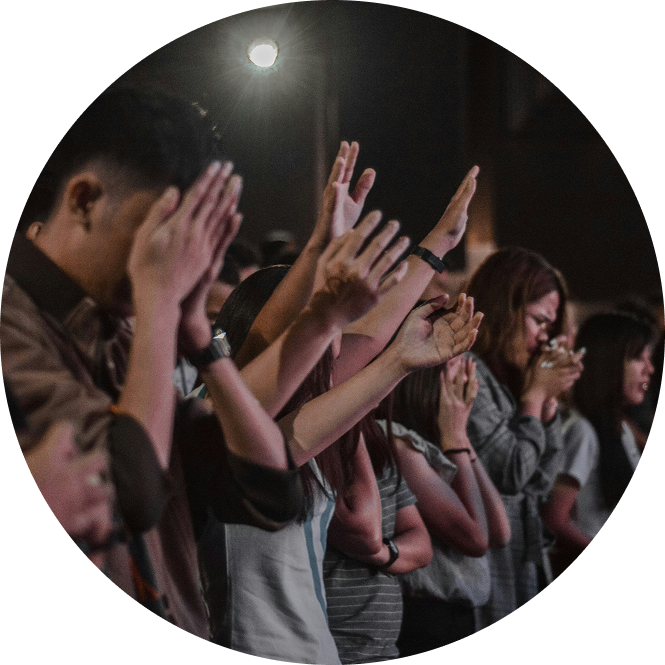 Audience with raised hands during a dimly lit concert or worship gathering