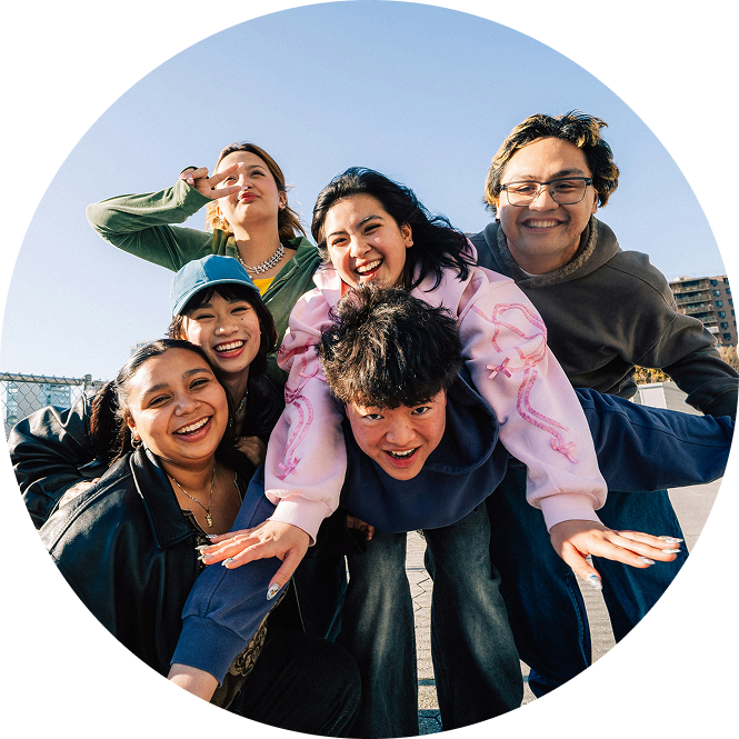 Five friends smiling and posing outdoors against a blue sky, one giving a piggyback ride