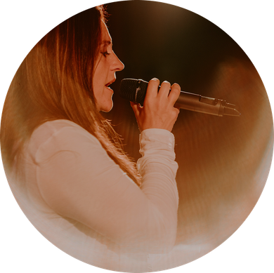 Side view of a singer with long hair holding a microphone under warm stage lights