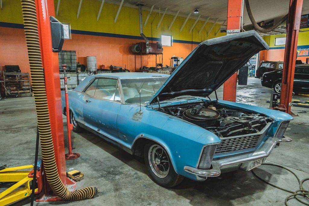 Blue car with open hood in a garage, on a lift.