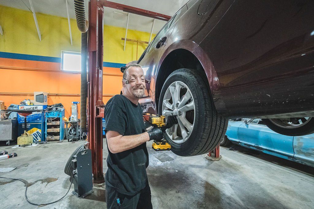 Mechanic working on car tire with a power tool, inside a garage.