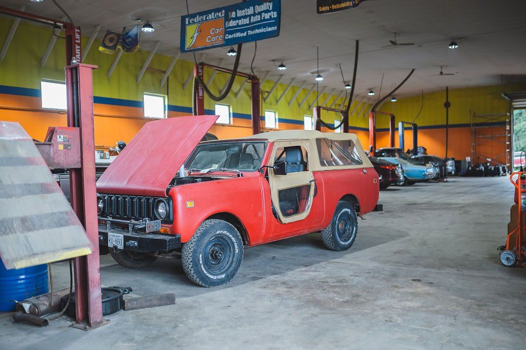 Red and beige vintage SUV with open hood in a garage.