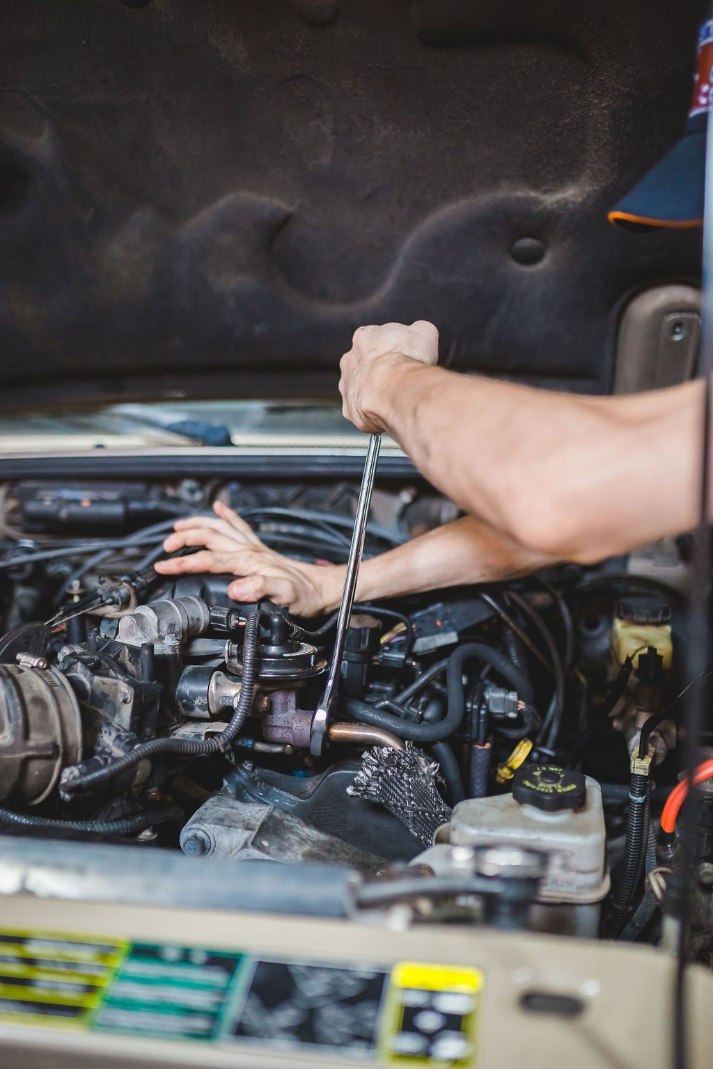Mechanic working on a car engine with a wrench. The hood is open in a garage setting.