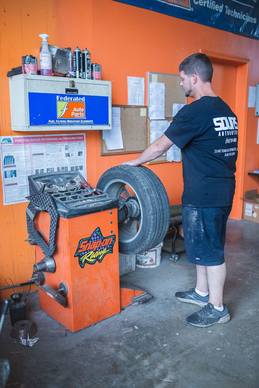 Mechanic balancing a tire on an orange machine in a garage.