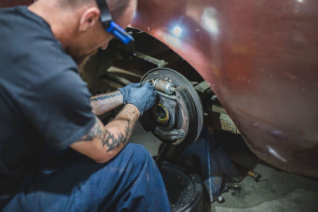 Mechanic working on car's brake system. Wearing a headlamp and gloves, in a garage.