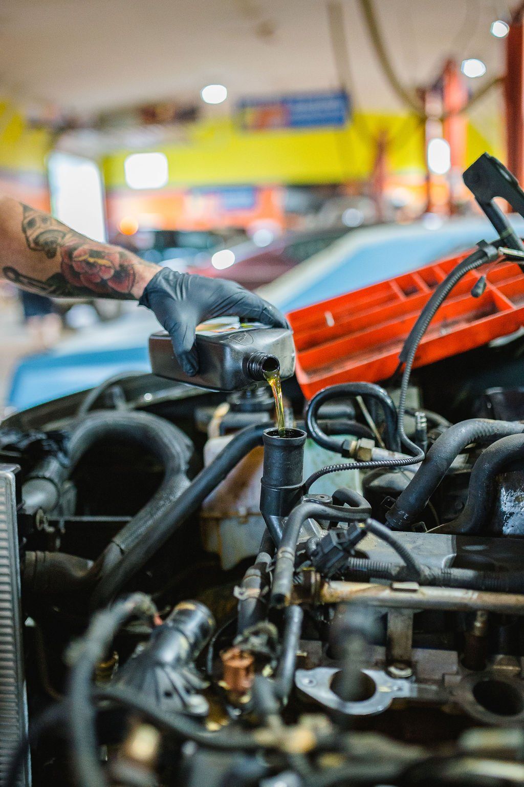 Person with tattoos adding fluid to a car engine in a garage.