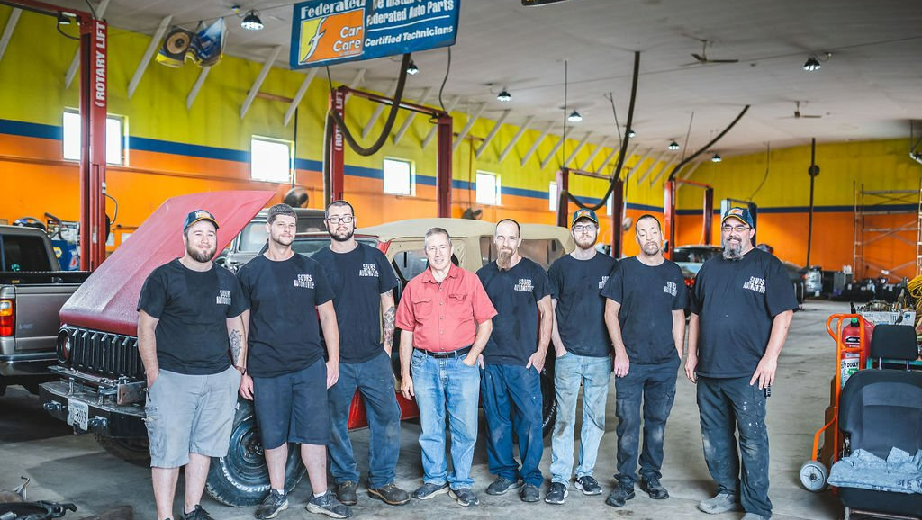 Group of mechanics posing in auto repair shop.