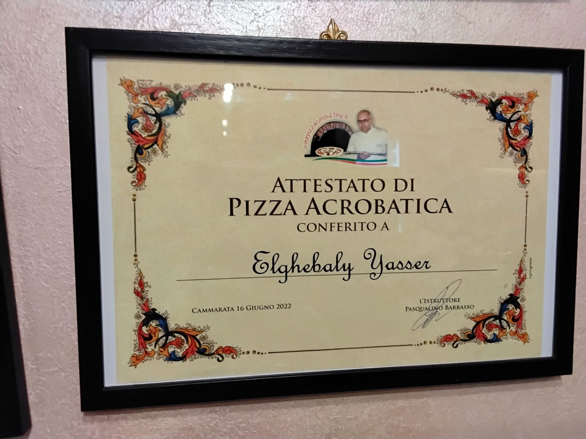Certificato incorniciato per acrobazie con la pizza, sfondo color crema con bordo floreale decorato su una parete