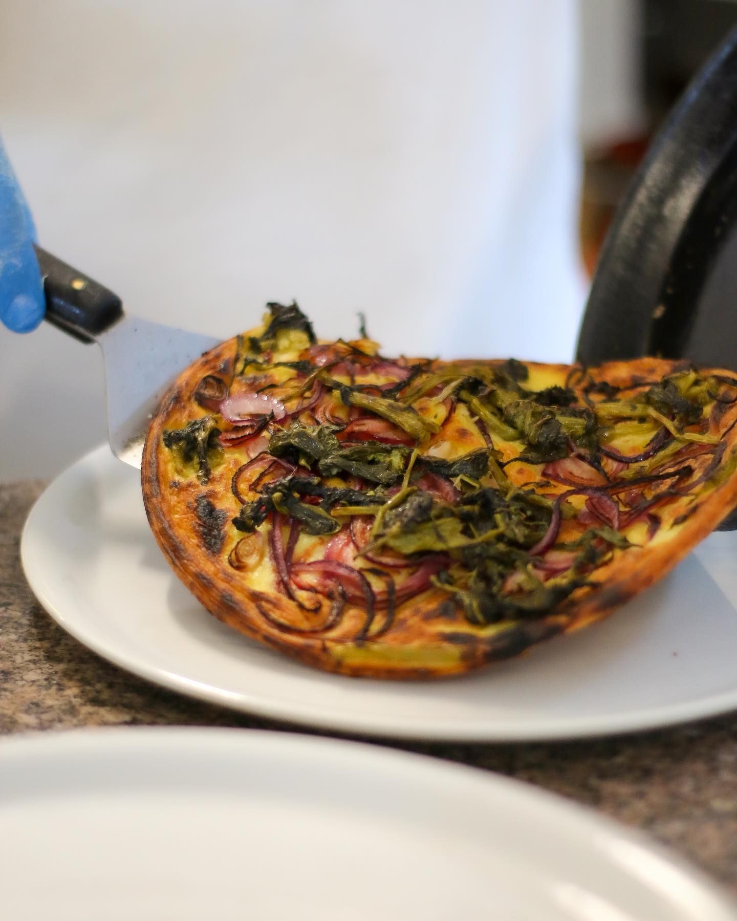 Una fetta di quiche con verdure viene tagliata su un piatto con un coltello.