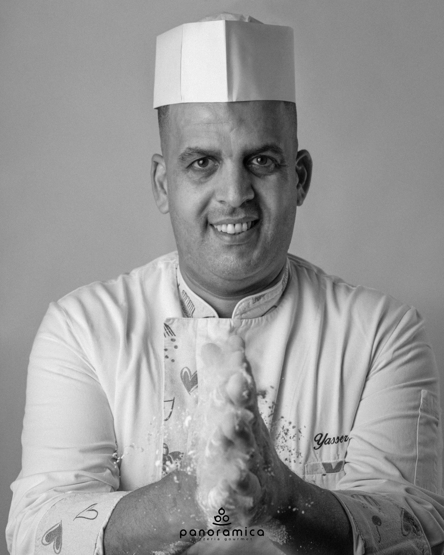 Ritratto di uno chef in uniforme e cappello bianchi, sorridente con le mani sporche di farina.