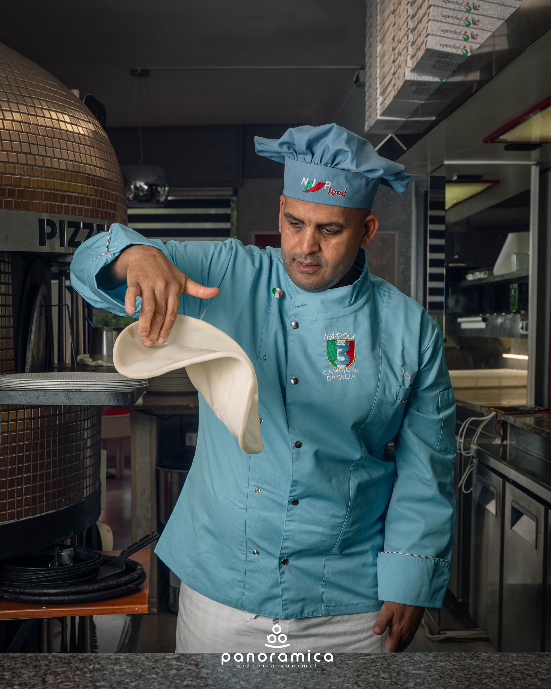 Uno chef in uniforme blu lancia l'impasto della pizza in cucina.