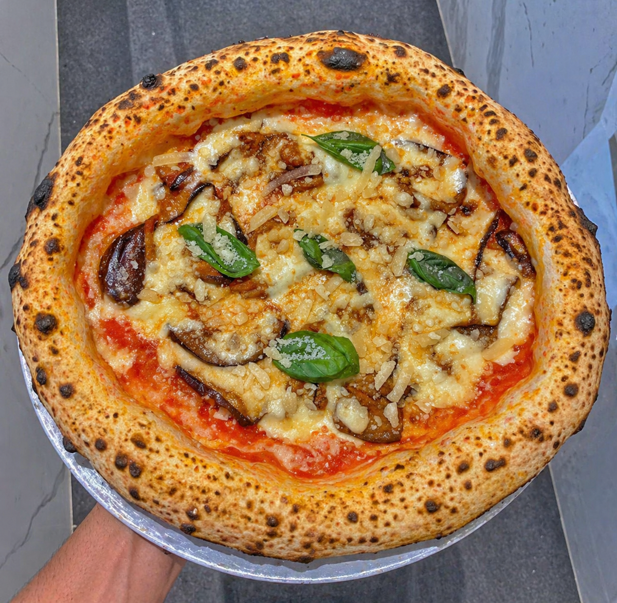 Pizza con foglie di basilico, funghi e formaggio fuso su una teglia di metallo, con una crosta dorata.