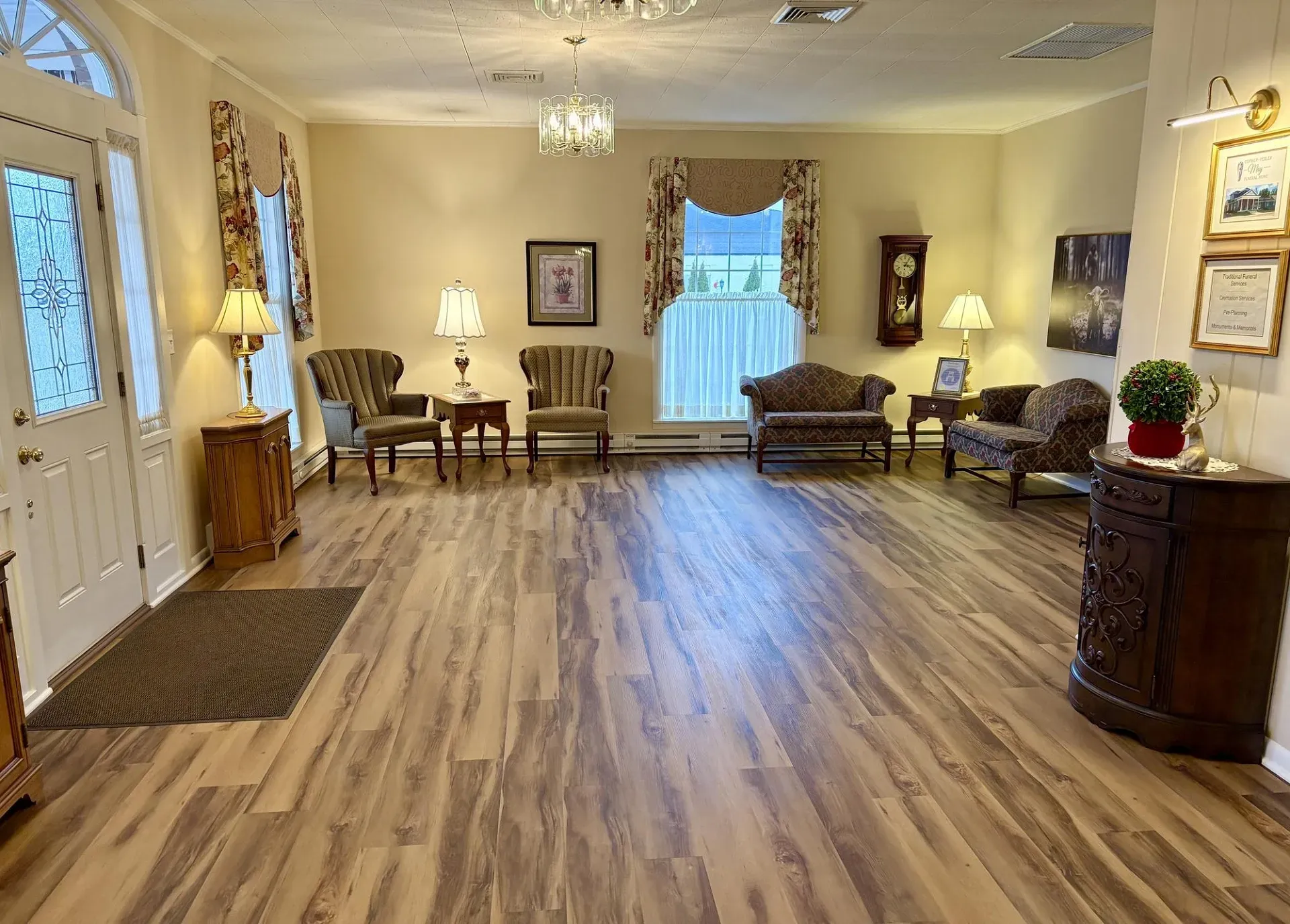 A waiting area with light-colored walls, wood floors, several armchairs, a sofa, and a corner cabinet in a classic style.