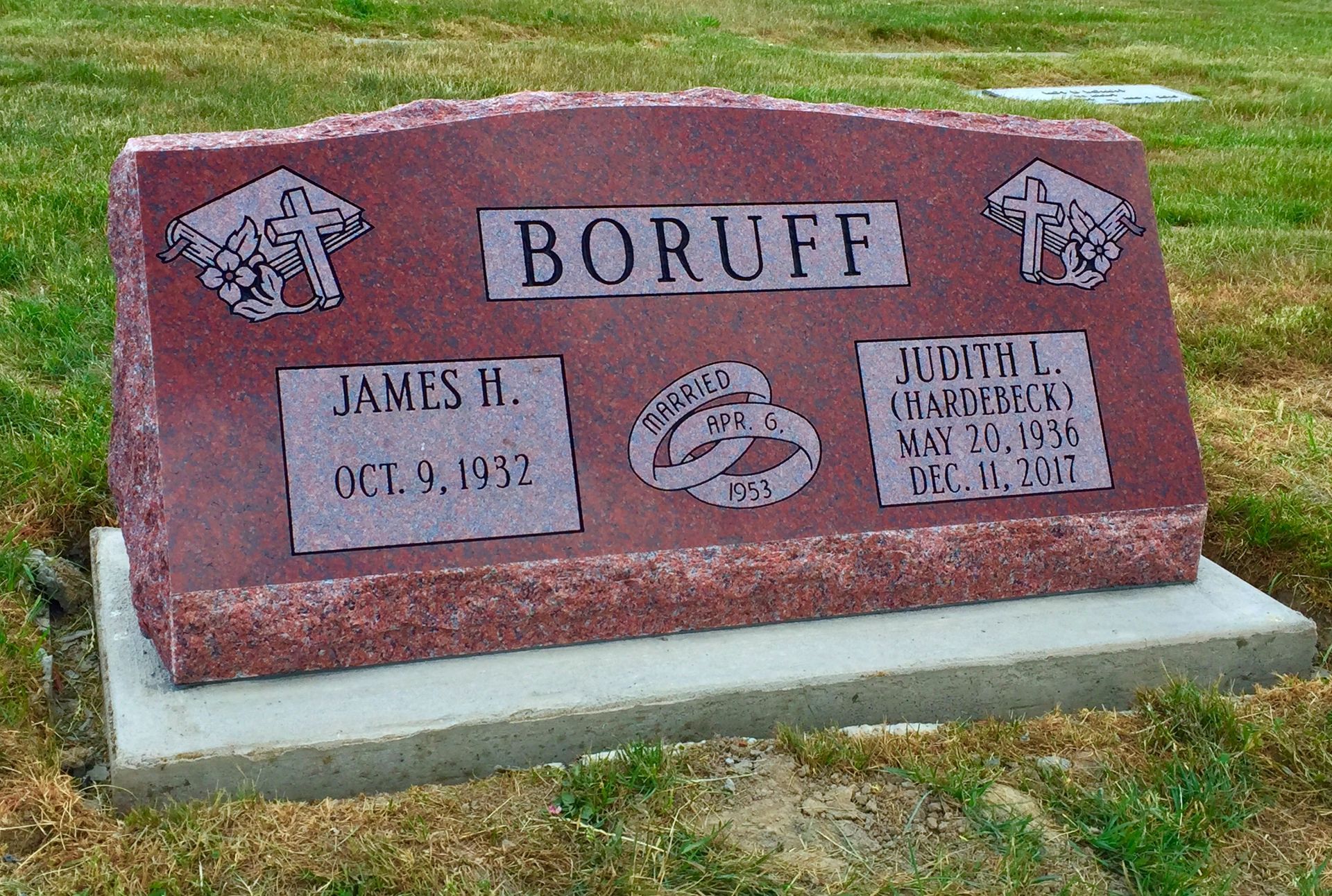Red granite gravestone for James H. and Judith L. Boruff, featuring etched wedding rings and crosses on a concrete base.