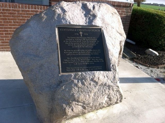 A granite memorial stone with an inset plaque for St. John's Chapel Church, located outside a brick building.