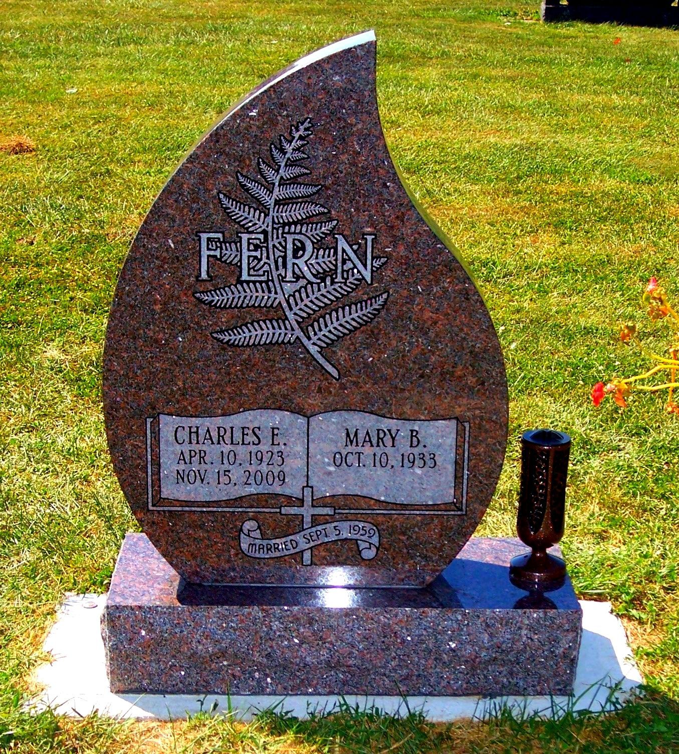 A tear-shaped granite headstone featuring an engraved fern, an open book, and the names Charles E. and Mary B. Fern.