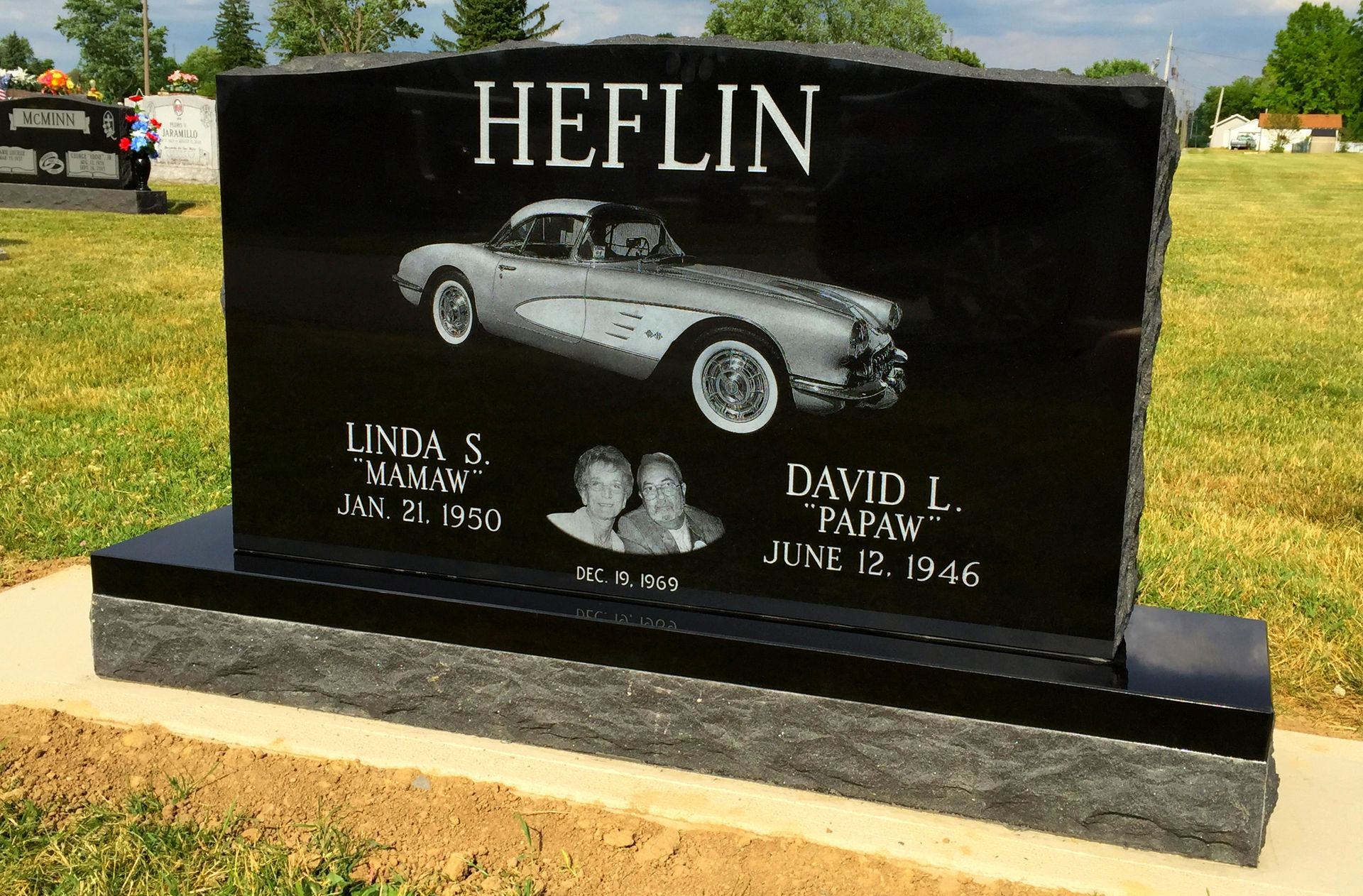 A black polished granite tombstone for the Heflin family, featuring an engraving of a classic convertible car.