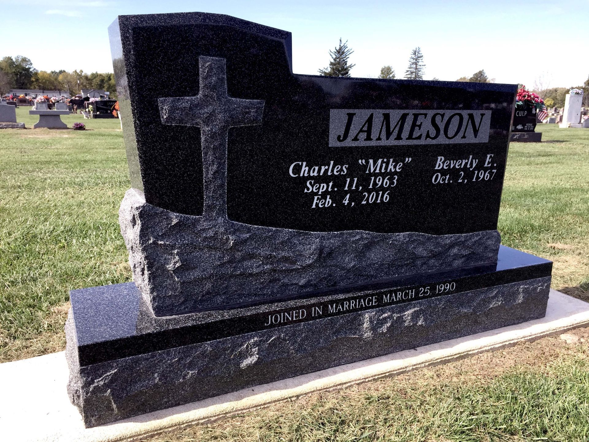 A black granite headstone with a cross engraving, reading