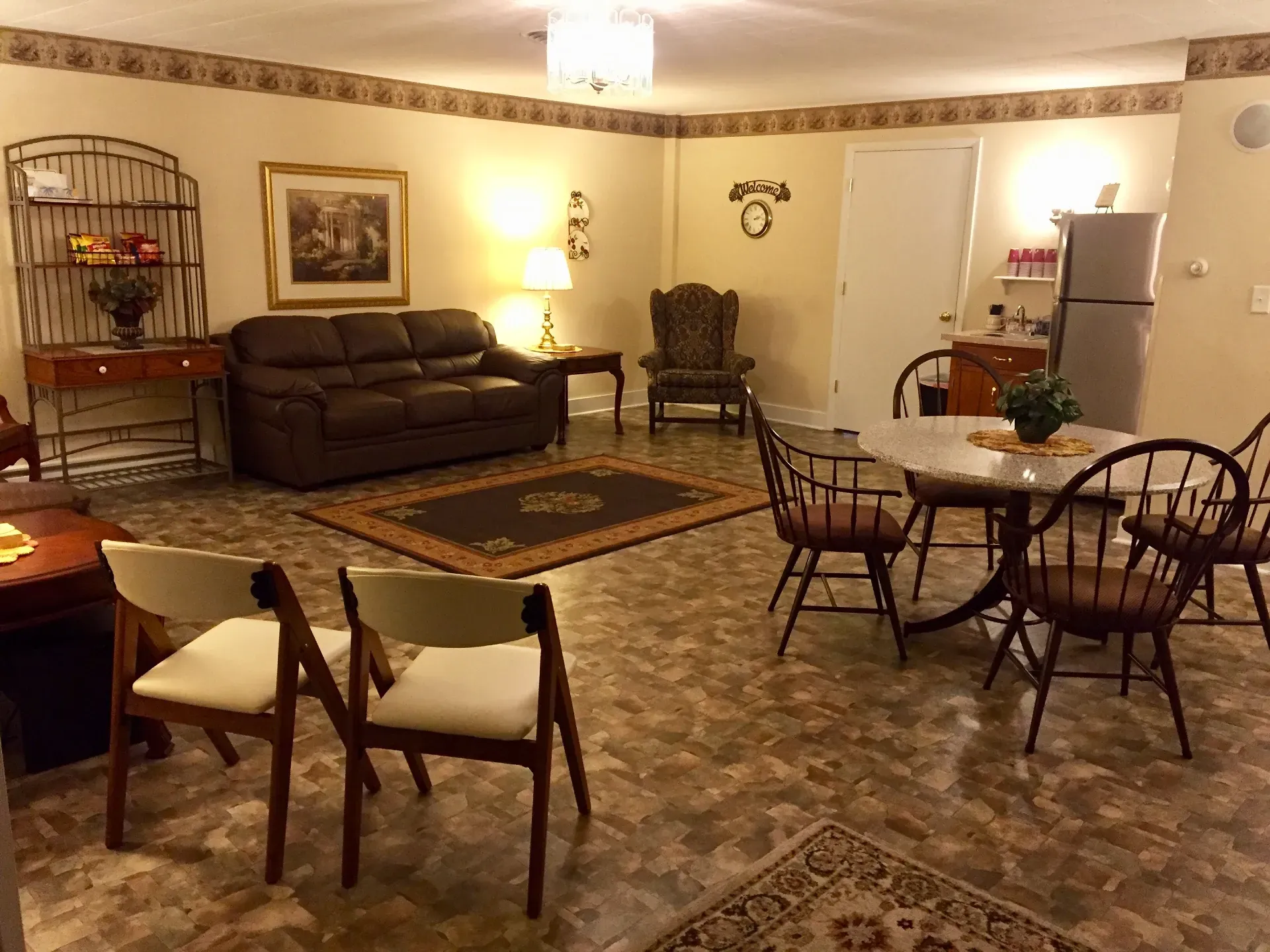 A living area with a brown sofa, armchairs, a dining table with chairs, a hutch, and tile flooring.