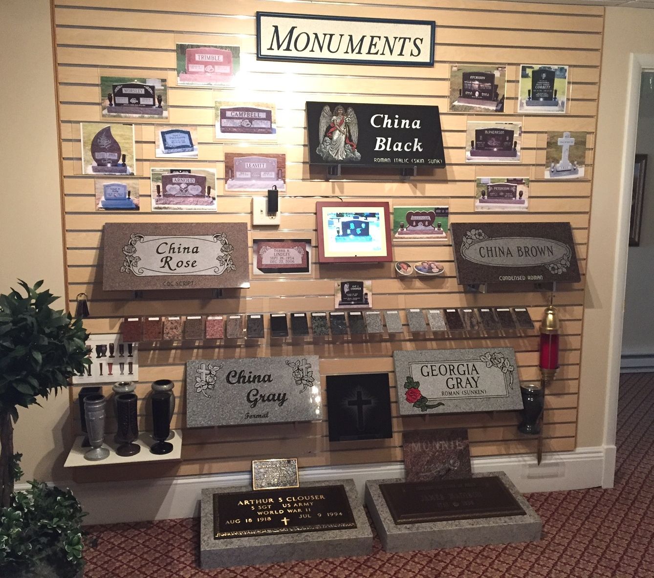 A display wall of various headstone and monument samples labeled by stone type, arranged on slatwall panels in a store.