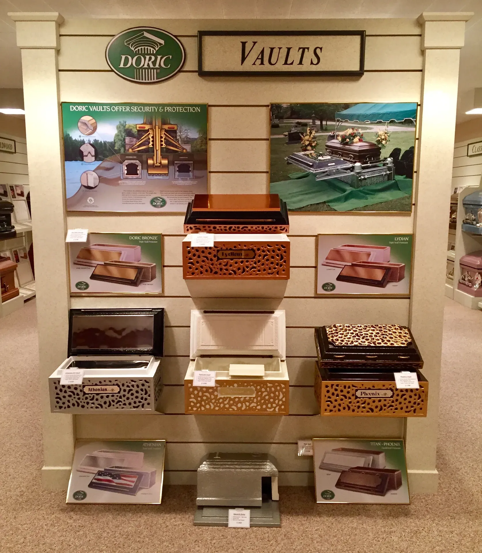 A retail display of burial vaults and related memorial products, arranged on shelves against a white wall.