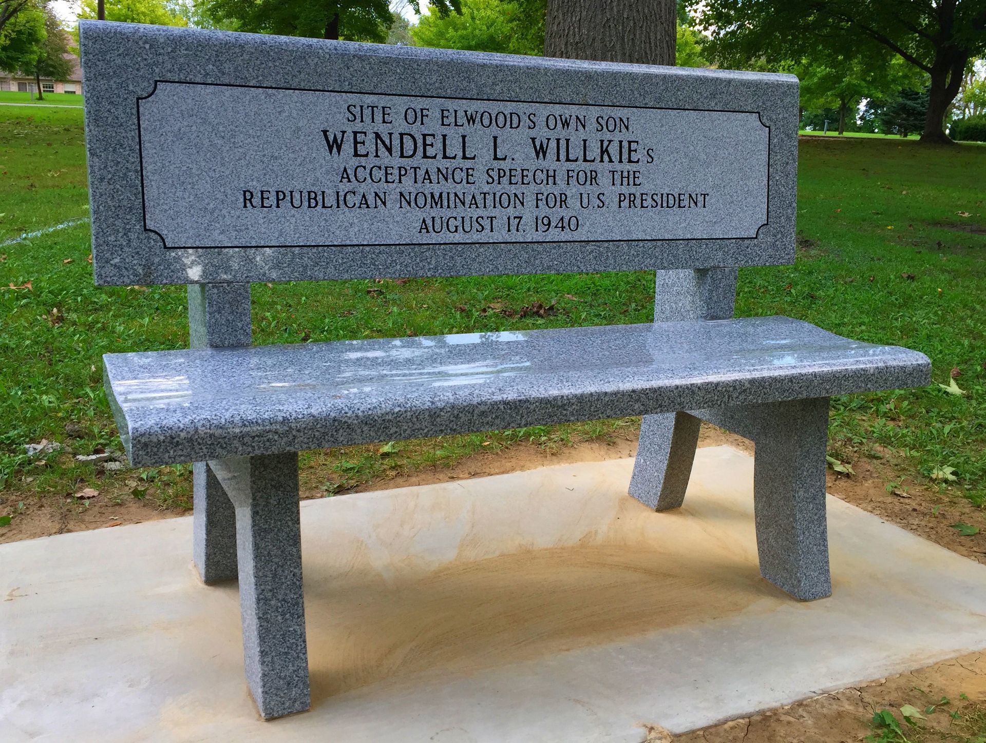 A grey granite memorial bench in a grassy park, engraved with text about Wendell L. Willkie’s 1940 acceptance speech.