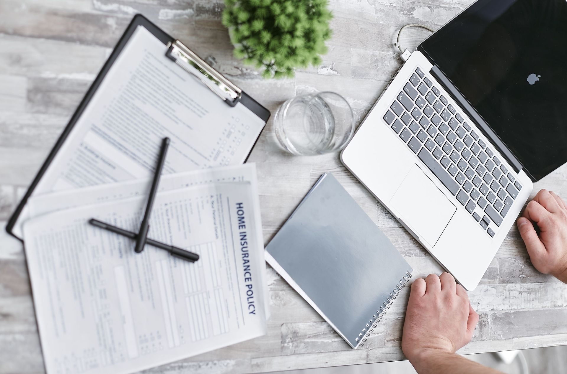 Overhead view of a desk with laptop, clipboard, notebook, coffee, and hands typing on a keyboard