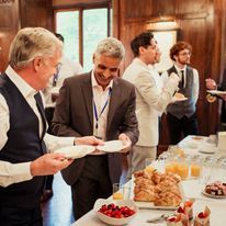 A group of men are standing around a table with plates of food.