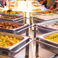 There are many trays of food on a table at a buffet.