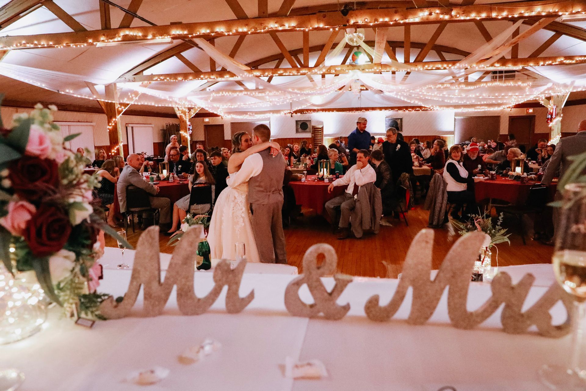 A bride and groom are dancing at their wedding reception in front of a mr. and mrs. sign.