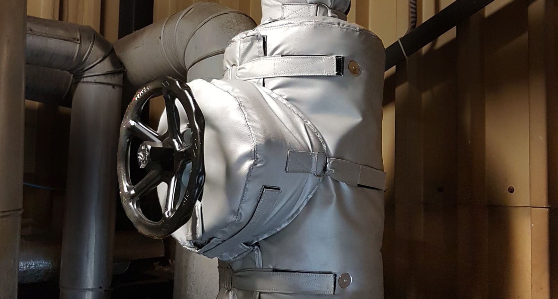 A valve with a blanket on it is surrounded by pipes in a room.