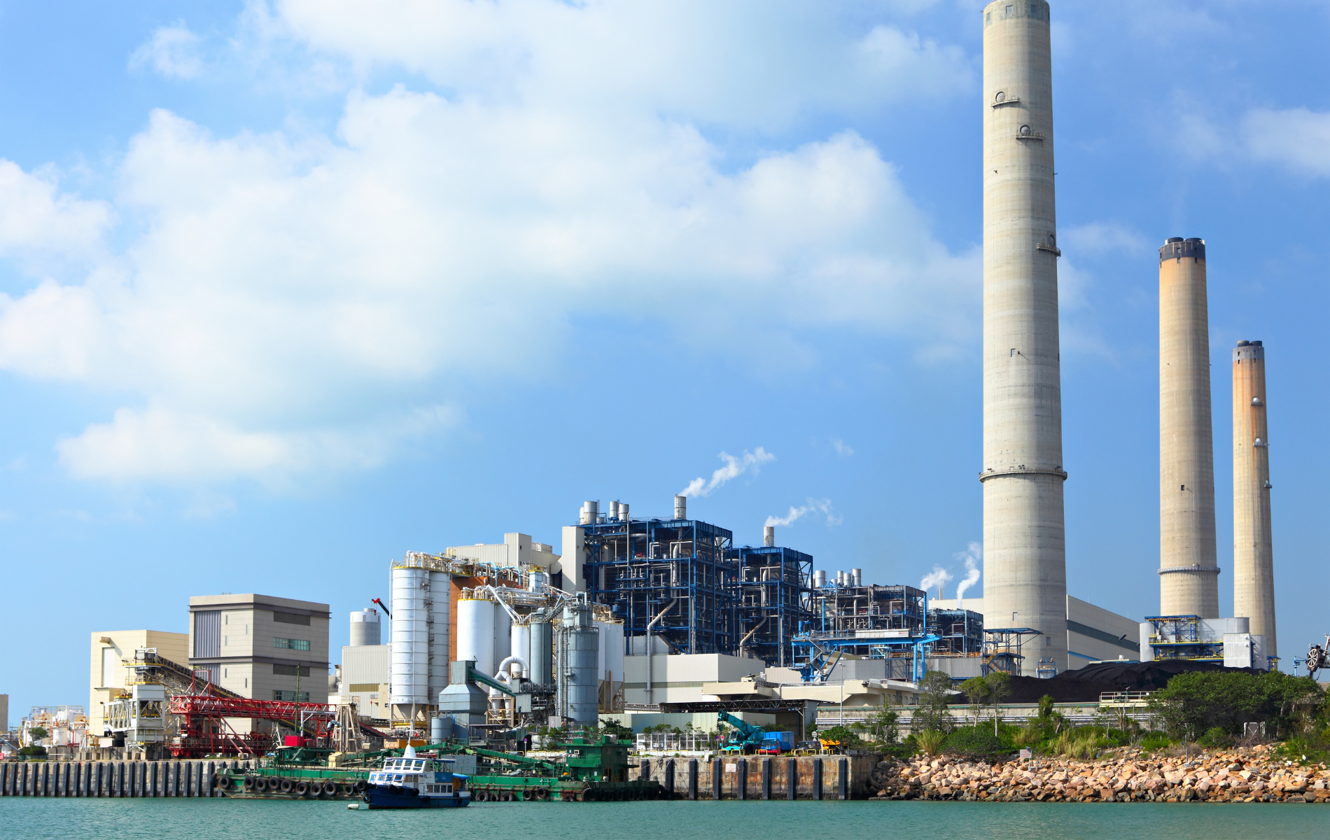 A large factory with a lot of chimneys next to a body of water.