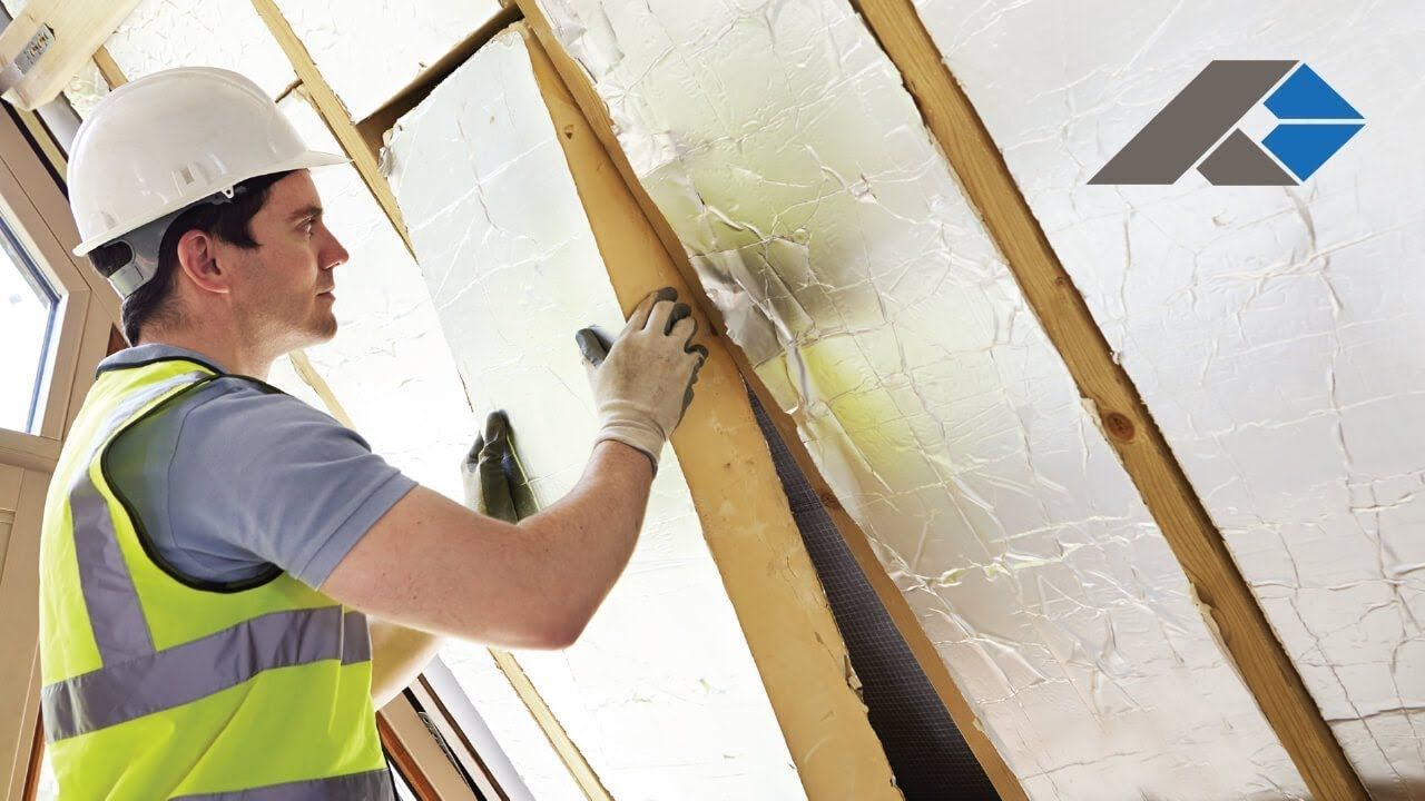 A man wearing a hard hat and safety vest is working on a wall.