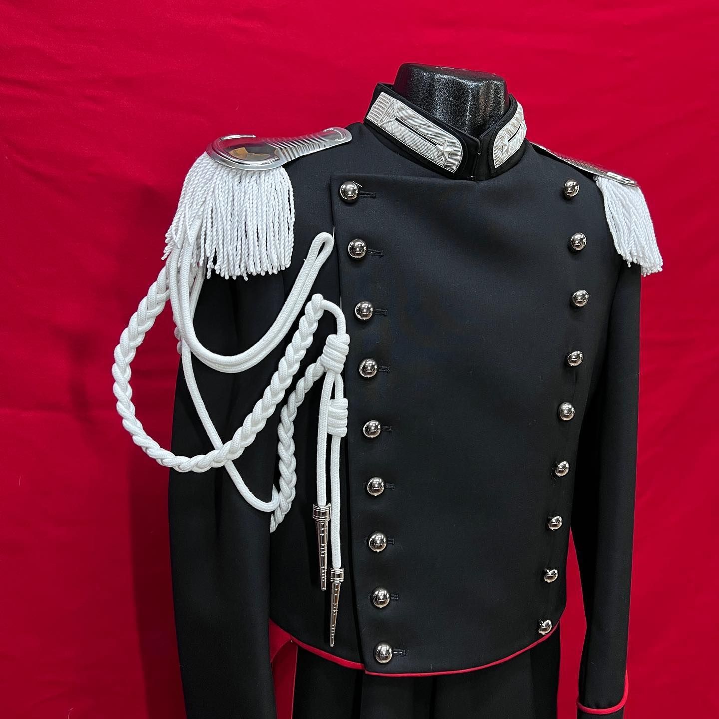 Giacca nera in stile militare con trecce e spalline argentate su sfondo rosso