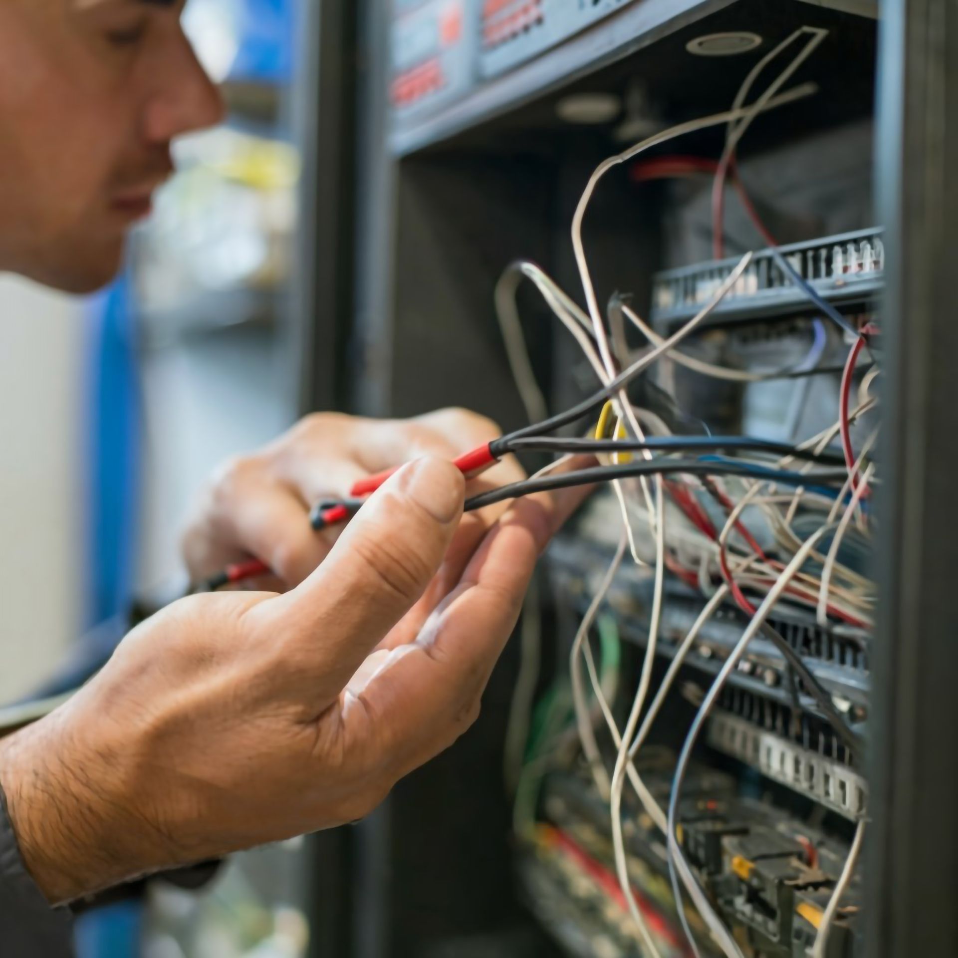 Man working on electrical wiring in a panel, holding wires with tools.